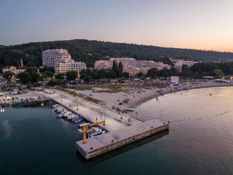Aerial view of Asparuhovo Fishing Marina with small boats docked at the pier sandy beach and residential buildings in the background at sunset in Varna Varna Bulgaria.