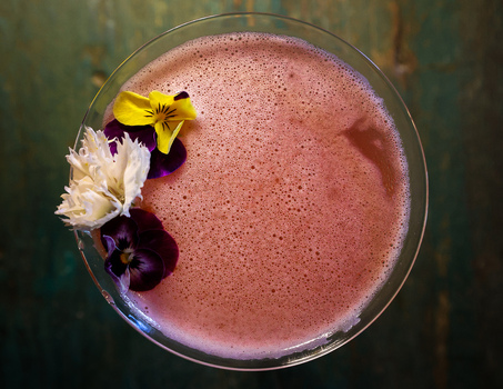 View of a pink cocktail in a glass garnished with edible yellow and purple pansies and a white carnation in San Jose del Cabo Baja California Sur Mexico.