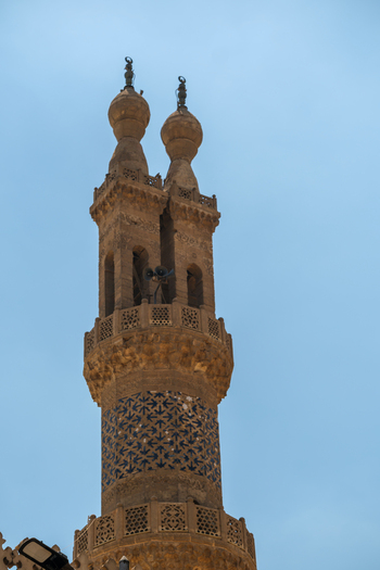 View of the ornate minaret of Al Azhar Mosque featuring intricate stone carvings and blue geometric patterns against a clear sky in Cairo Egypt. View of the ornate minaret of Al Azhar Mosque featuring intricate stone carvings and blue geometric patterns against a clear sky in Cairo Egypt.