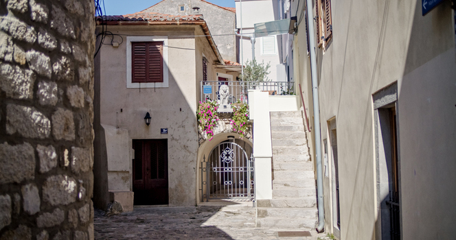 Krk Primorje Gorski Kotar Croatia 19 September 2026 View of a narrow cobblestone street in the old town with stone buildings a stone staircase a metal gate and pink flowers. Krk Primorje Gorski Kotar Croatia 19 September 2026 View of a narrow cobblestone street in the old town with stone buildings a stone staircase a metal gate and pink flowers.