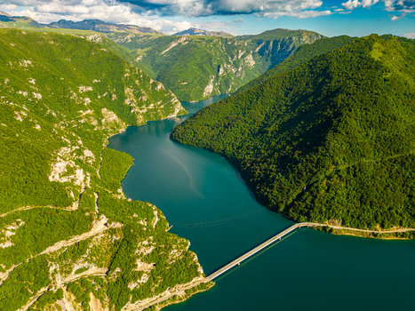 Aerial view of Piva Lake with its turquoise water and a bridge crossing the canyon surrounded by lush green mountains in Pluzine Municipality Montenegro. Aerial view of Piva Lake with its turquoise water and a bridge crossing the canyon surrounded by lush green mountains in Pluzine Municipality Montenegro.