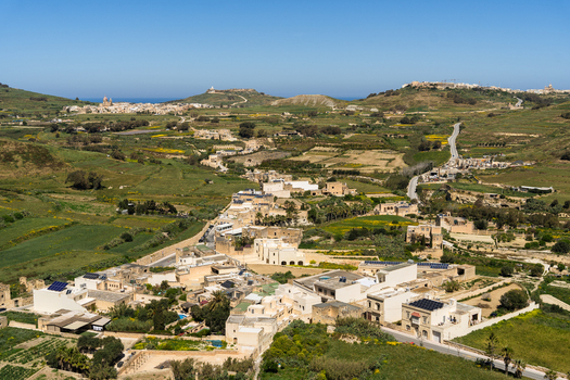 View of traditional limestone houses and lush green fields under a clear blue sky in the rural landscape of Zebbug Gozo Region Malta. View of traditional limestone houses and lush green fields under a clear blue sky in the rural landscape of Zebbug Gozo Region Malta.