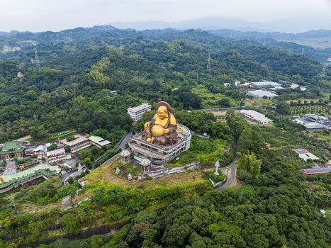 Aerial view of the large golden Laughing Buddha statue surrounded by lush green forests and temple buildings in Jiuru Township Pingtung County Taiwan. Aerial view of the large golden Laughing Buddha statue surrounded by lush green forests and temple buildings in Jiuru Township Pingtung County Taiwan.