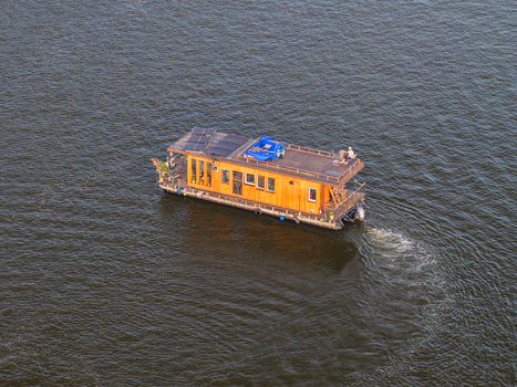 Aerial view of a wooden houseboat cruising on the Spree river with solar panels on the roof near Treptower Park in Berlin Berlin Germany. Aerial view of a wooden houseboat cruising on the Spree river with solar panels on the roof near Treptower Park in Berlin Berlin Germany.