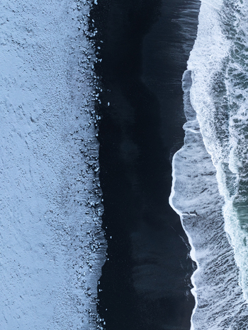 Aerial view of Diamond Beach with scattered ice chunks on black volcanic sand and ocean waves crashing on the shore Sveitarfelagid Hornaf Iceland.