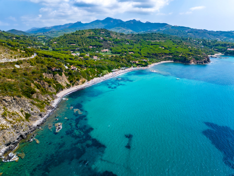 Aerial view of the turquoise waters and sandy beach of Capoliveri surrounded by lush green hills and rocky cliffs in Capoliveri Tuscany Italy.