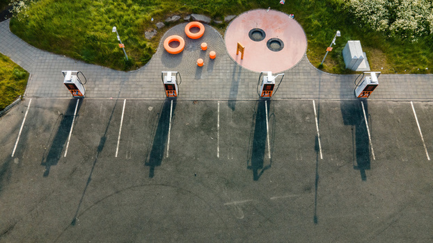 Reykjavik Iceland 05 July 2026 Aerial view of an electric vehicle charging station in a parking lot with long shadows green grass and orange circular elements.
