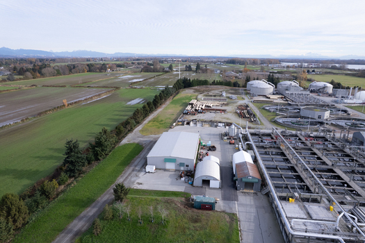 Aerial view of the wastewater treatment plant featuring circular tanks and industrial buildings surrounded by agricultural fields in Richmond British Columbia Canada. Aerial view of the wastewater treatment plant featuring circular tanks and industrial buildings surrounded by agricultural fields in Richmond British Columbia Canada.