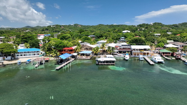Aerial view of West End with its coastal docks boats moored in turquoise water and buildings nestled against lush green hills in West End Bay Islands Department Honduras. Aerial view of West End with its coastal docks boats moored in turquoise water and buildings nestled against lush green hills in West End Bay Islands Department Honduras.