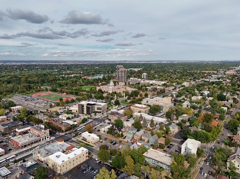 Aerial view of the urban landscape of Denver featuring residential areas a sports field and green trees under a partly cloudy sky in Denver Colorado United States. Aerial view of the urban landscape of Denver featuring residential areas a sports field and green trees under a partly cloudy sky in Denver Colorado United States.