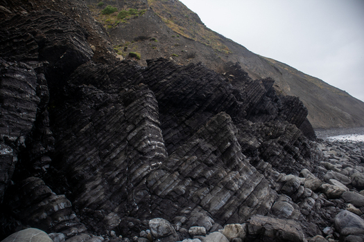 View of dramatic dark tilted layered rock formations and steep coastal cliffs along the rugged shoreline of the Lost Coast Humboldt County California United States.