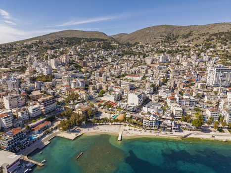 Aerial view of the coastal city of Saranda with its dense urban architecture beach and harbor nestled against rolling hills along the Ionian Sea in Saranda Vlore County Albania. Aerial view of the coastal city of Saranda with its dense urban architecture beach and harbor nestled against rolling hills along the Ionian Sea in Saranda Vlore County Albania.