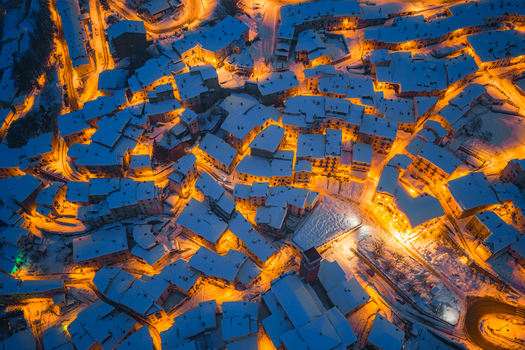 Aerial view of the snow covered town of Rivisondoli at night with warm streetlights illuminating the rooftops and narrow streets in Rivisondoli Abruzzo Italy.