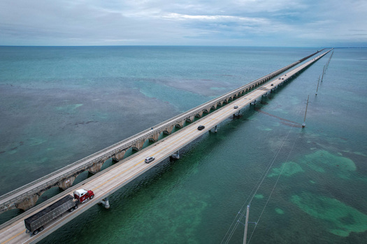 Aerial view of The Overseas Highway stretching across turquoise waters with vehicles driving under a cloudy sky in Key Largo Florida United States. Aerial view of The Overseas Highway stretching across turquoise waters with vehicles driving under a cloudy sky in Key Largo Florida United States.