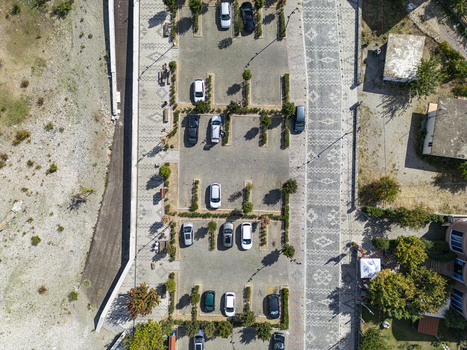 Aerial view of a paved parking lot with various cars parked in designated spaces surrounded by stone pathways and greenery in Shiroke Qarku i Shkodres Albania. Aerial view of a paved parking lot with various cars parked in designated spaces surrounded by stone pathways and greenery in Shiroke Qarku i Shkodres Albania.