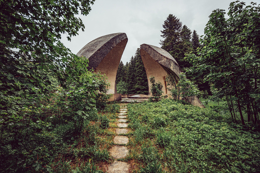 View of the Korcanica Memorial Zone monument with curved concrete structures and a stone path surrounded by lush forest and trees Sanski Most Federation of Bosnia Bosnia and Herzegovina. View of the Korcanica Memorial Zone monument with curved concrete structures and a stone path surrounded by lush forest and trees Sanski Most Federation of Bosnia Bosnia and Herzegovina.