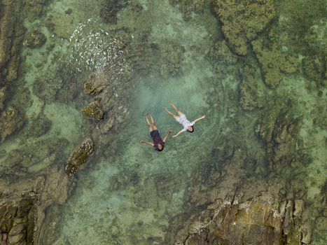 Aerial view of two people floating in the clear turquoise waters surrounded by rugged rocks at Annora beach Karimunjawa Jawa Tengah Indonesia.