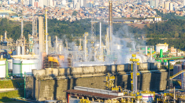 Aerial view of the petrochemical complex with industrial cooling towers processing units and smoke plumes set against an urban background in Santo Andre State of Sao Paulo Brazil.