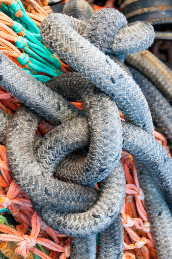 View of weathered grey fishing ropes knotted together over vibrant orange and green netting in Canada. View of weathered grey fishing ropes knotted together over vibrant orange and green netting in Canada.