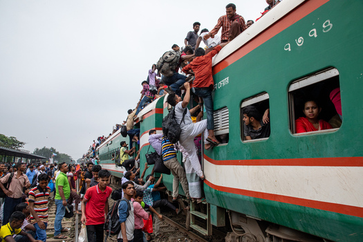 Dhaka Bangladesh 15 June 2018 View of the Airport Railway Station with people climbing on the roof and hanging from the doors of a crowded green and red train. Dhaka Bangladesh 15 June 2018 View of the Airport Railway Station with people climbing on the roof and hanging from the doors of a crowded green and red train.