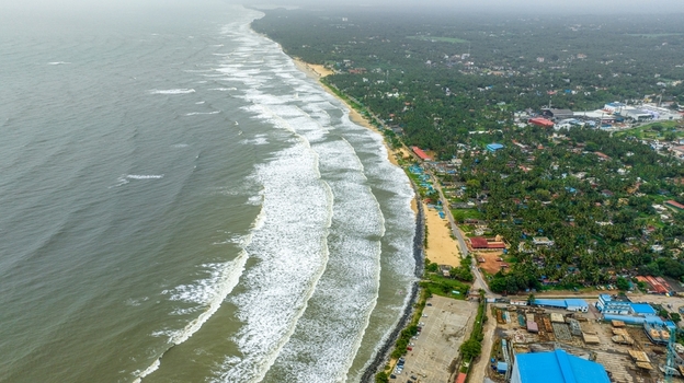 Aerial view of Malpe Fishing Harbour with waves crashing on the sandy beach lush palm trees and coastal infrastructure in Udupi Karnataka India. Aerial view of Malpe Fishing Harbour with waves crashing on the sandy beach lush palm trees and coastal infrastructure in Udupi Karnataka India.