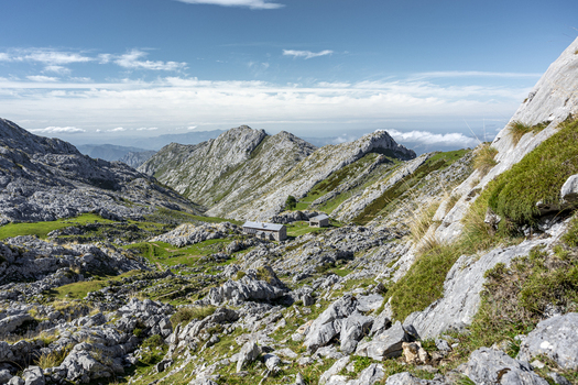 View of a rugged rocky landscape with a small stone building nestled amidst green patches under a vast sky with scattered clouds Picos de Europa Asturias Spain.