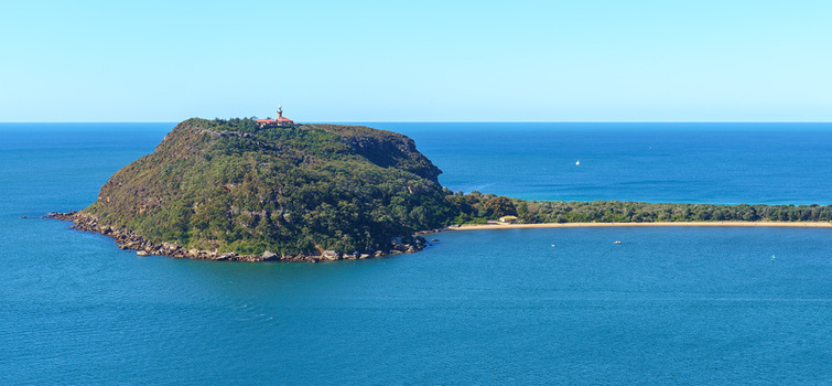 View of Barrenjoey Head with its historic lighthouse lush greenery and sandy beach surrounded by the blue waters of the Tasman Sea in Palm Beach New South Wales Australia.