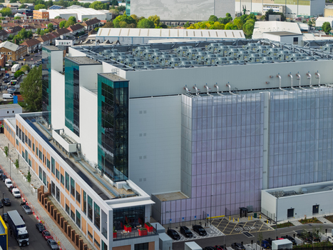 Aerial view of a large modern data center with rooftop cooling units glass facade and surrounding urban infrastructure in the United Kingdom. Aerial view of a large modern data center with rooftop cooling units glass facade and surrounding urban infrastructure in the United Kingdom.