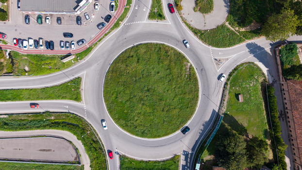 Aerial view of a roundabout with cars driving on the asphalt road and a green grassy center surrounded by parking spaces and trees in Milan Lombardy Italy.