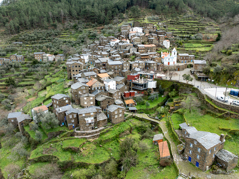 Aerial view of stone houses cascade down the terraced slopes crowned by a white church a timeless village nestled in verdant hills Piódão Arganil Portugal. Aerial view of stone houses cascade down the terraced slopes crowned by a white church a timeless village nestled in verdant hills Piódão Arganil Portugal.