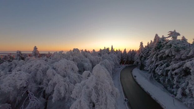 FPV aerial view of snowy forest road at sunset Germany.