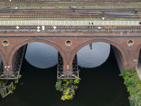 Aerial view of a historic brick arch bridge with railway tracks running across the top spanning a calm river with green vegetation growing on the stone piers Poland. Aerial view of a historic brick arch bridge with railway tracks running across the top spanning a calm river with green vegetation growing on the stone piers Poland.