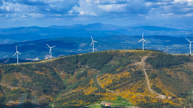Aerial view of wind turbines situated on rolling hills covered with green forests and yellow wildflowers under a bright blue sky in Lisbon Lisbon Portugal. Aerial view of wind turbines situated on rolling hills covered with green forests and yellow wildflowers under a bright blue sky in Lisbon Lisbon Portugal.