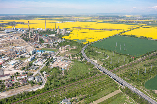 Aerial view of an industrial plant with tall chimneys and cooling towers next to bright yellow rapeseed fields and a highway bridge in Ploiesti Prahova Romania. Aerial view of an industrial plant with tall chimneys and cooling towers next to bright yellow rapeseed fields and a highway bridge in Ploiesti Prahova Romania.