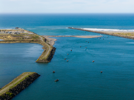 Aerial view of salmon fishing boats navigating the river mouth at the Pacific Ocean in Gold Beach Oregon United States.