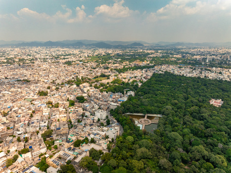 Aerial view of the sprawling urban landscape of Udaipur featuring dense residential buildings and a lush green forest area with a small water body Udaipur Rajasthan India. Aerial view of the sprawling urban landscape of Udaipur featuring dense residential buildings and a lush green forest area with a small water body Udaipur Rajasthan India.