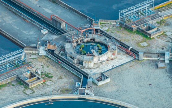 Aerial view of wastewater treatment channels pumping infrastructure and circular processing equipment at an industrial water treatment facility in Italy.