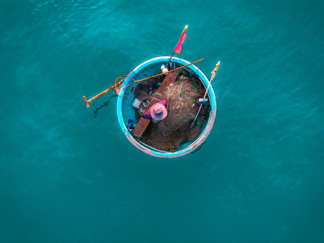 Aerial view of a traditional round basket boat with a fisherman sorting fishing nets in the turquoise waters of Vietnam. Aerial view of a traditional round basket boat with a fisherman sorting fishing nets in the turquoise waters of Vietnam.