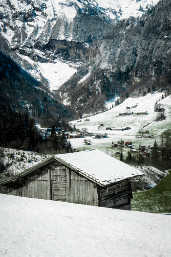 View of a quaint wooden cabin dusted with snow nestled against a backdrop of towering snow covered mountains Train from Lucerne to Interlaken Switzerland. View of a quaint wooden cabin dusted with snow nestled against a backdrop of towering snow covered mountains Train from Lucerne to Interlaken Switzerland.
