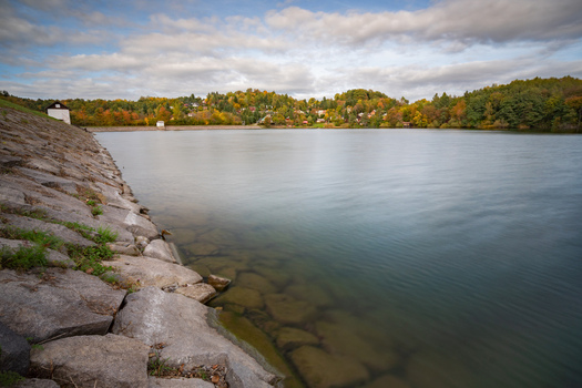 View of Velka Richnava lake with a stone embankment in the foreground and autumn trees under a cloudy sky in Stiavnicke Bane Banska Bystrica Region Slovakia.