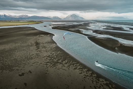 Aerial view of a kitesurfer gliding across the shallow tidal waters near the dramatic Vestrahorn mountain range under a cloudy sky in Sveitarfelagid Hornafjordur Iceland. Aerial view of a kitesurfer gliding across the shallow tidal waters near the dramatic Vestrahorn mountain range under a cloudy sky in Sveitarfelagid Hornafjordur Iceland.