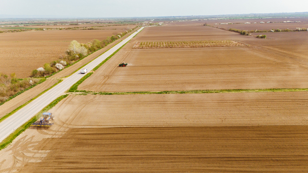 Aerial view of tractors working the vast ploughed fields creating linear patterns contrasting with the adjacent lush green vegetation Sremska Mitrovica Vojvodina Serbia. Aerial view of tractors working the vast ploughed fields creating linear patterns contrasting with the adjacent lush green vegetation Sremska Mitrovica Vojvodina Serbia.