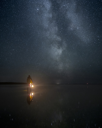 Laane County Estonia 06 September 2024 View of a person holding a lantern in shallow water under a starry night sky with the Milky Way reflecting on the surface on Vormsi island.