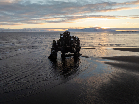 Aerial view of the Hvitserkur basalt sea stack on a black sand beach at sunset with calm water and distant snow capped mountains Iceland. Aerial view of the Hvitserkur basalt sea stack on a black sand beach at sunset with calm water and distant snow capped mountains Iceland.