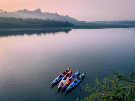 View of four colorful kayaks floating on a calm river with misty hills and lush green forests in the background during a soft sunrise Cox s Bazar Chittagong Division Bangladesh. View of four colorful kayaks floating on a calm river with misty hills and lush green forests in the background during a soft sunrise Cox s Bazar Chittagong Division Bangladesh.