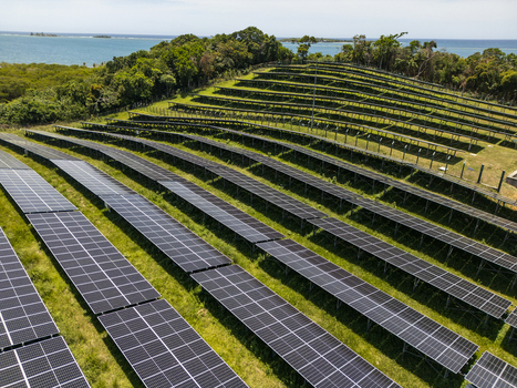 Aerial view of a large solar panel farm installed on a lush green hillside overlooking the turquoise Caribbean Sea in Guanaja Bay Islands Department Honduras.