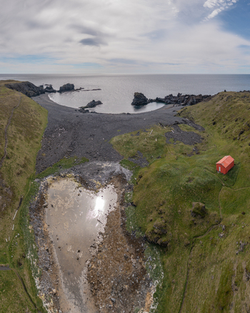 Aerial view of Djupalonssandur beach featuring a striking black sand coastline a small red building nestled on the grassy cliff and a reflective pool in Iceland. Aerial view of Djupalonssandur beach featuring a striking black sand coastline a small red building nestled on the grassy cliff and a reflective pool in Iceland.