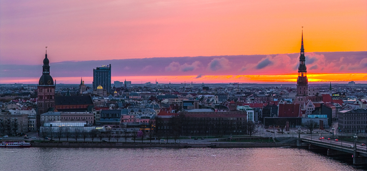 Aerial view of the historic skyline of Riga featuring St. Peter s Church and Riga Cathedral at sunset with a vibrant orange and purple sky over the Daugava River in Riga Latvia. Aerial view of the historic skyline of Riga featuring St. Peter s Church and Riga Cathedral at sunset with a vibrant orange and purple sky over the Daugava River in Riga Latvia.
