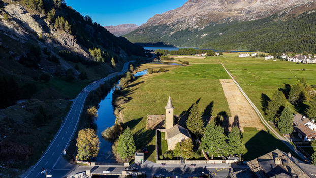Aerial view of the historic Church of San Lorenzo surrounded by lush green meadows a winding river and a mountain road in Sils im EngadinSegl Grisons Switzerland.
