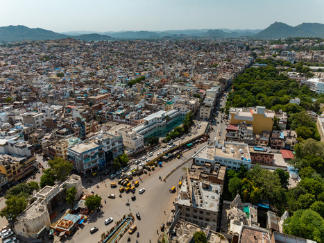 Aerial view of the historic city of Udaipur featuring dense urban architecture bustling streets with traffic and lush green trees bordering the cityscape in Udaipur Rajasthan India.